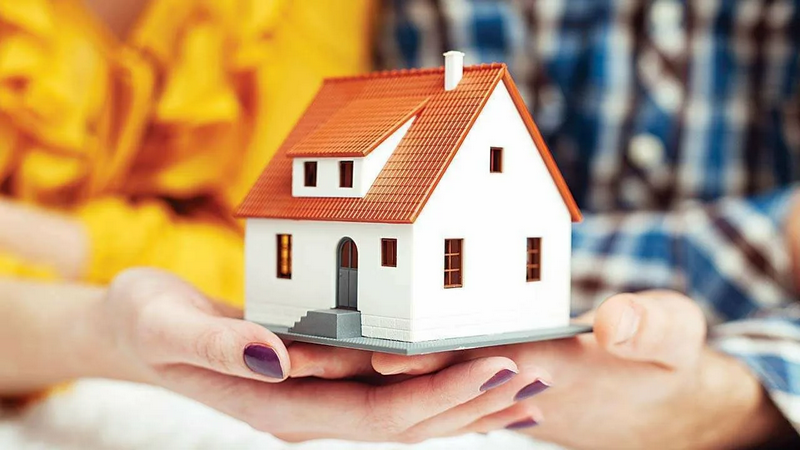 A pair of hands holding a small model of a house with a red roof.